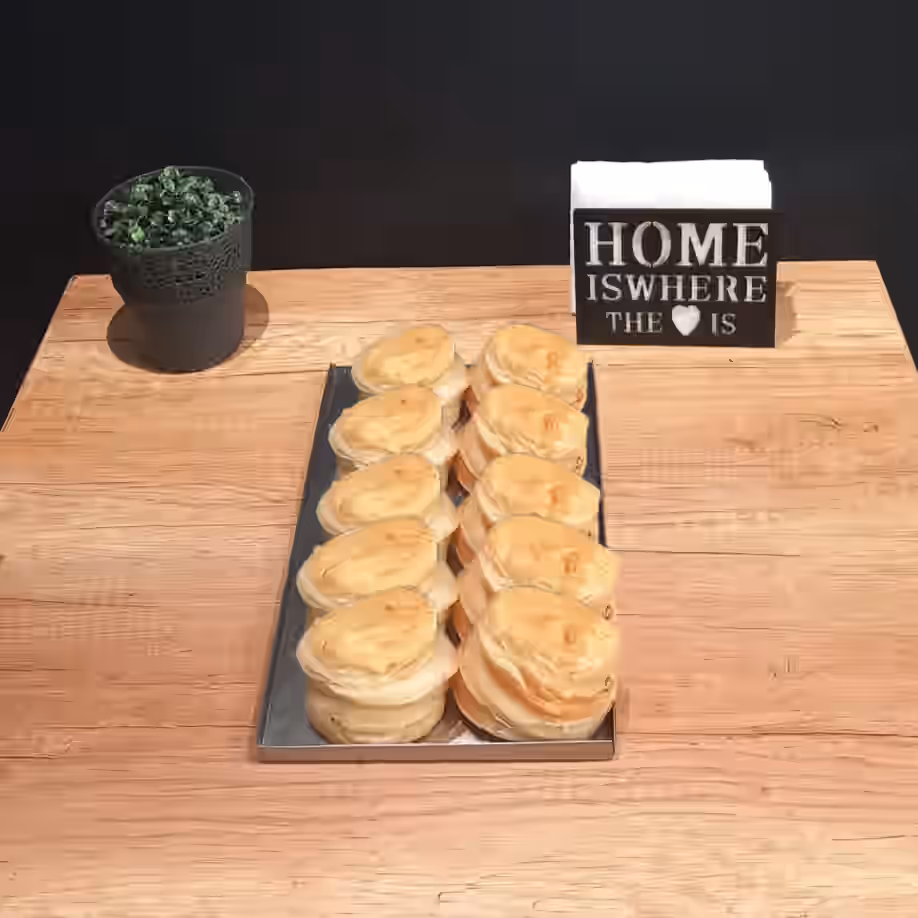 Tray with two rows of heart-shaped pastries on a wooden table, with a small potted plant on the left and a tissue holder with the phrase 'Home is where the ♥ is' on the right.